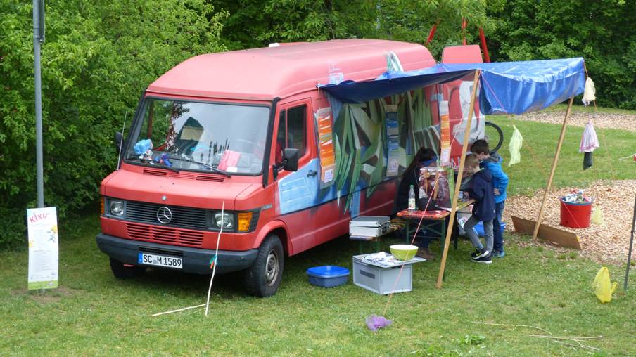 Das alte rote Spielmobil mit aufgebautem Vordach aus einer Plane.
