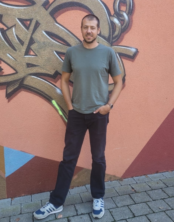 Foto von Maximilian Teichmann vor einem Graffiti an der Fassade des Aurex
