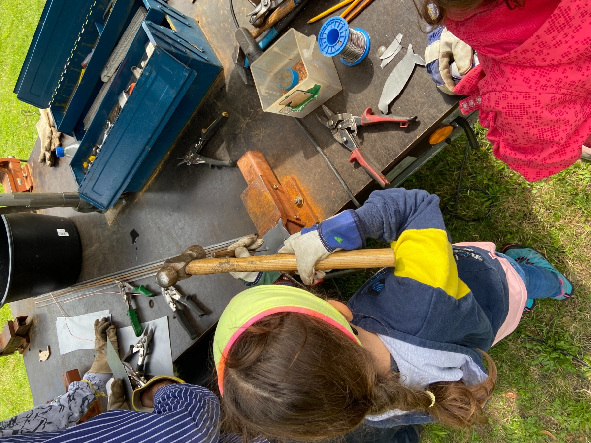 Ein Kind schlägt mit Hammer und Meisel Muster in ein Stück Metall.