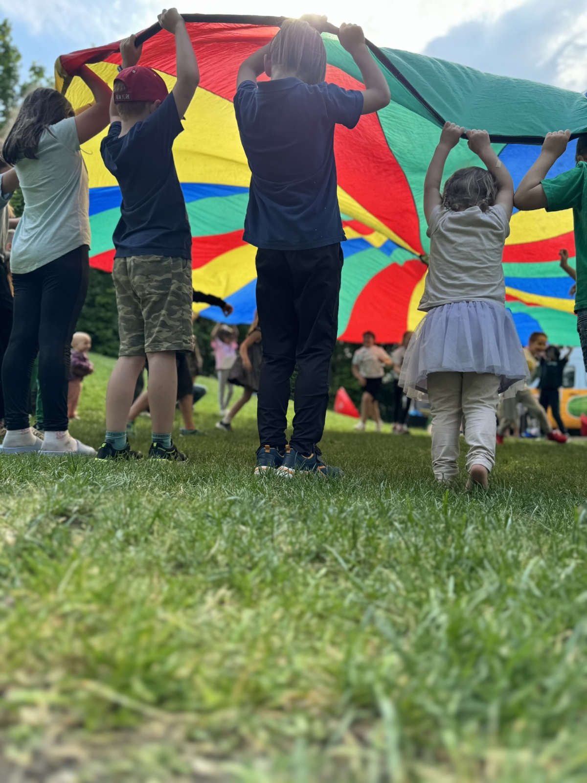 Zu sehen sind Kinder, die den bunten Fallschirm schwingen und ein Spiel spielen.