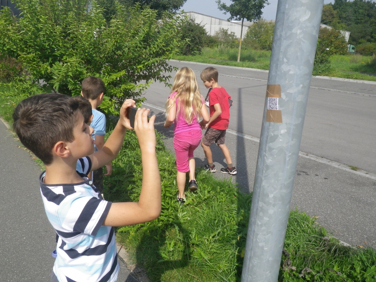 Ein Kind scannt einen QR-Code mit einem Smartphone auf einer Laterne.